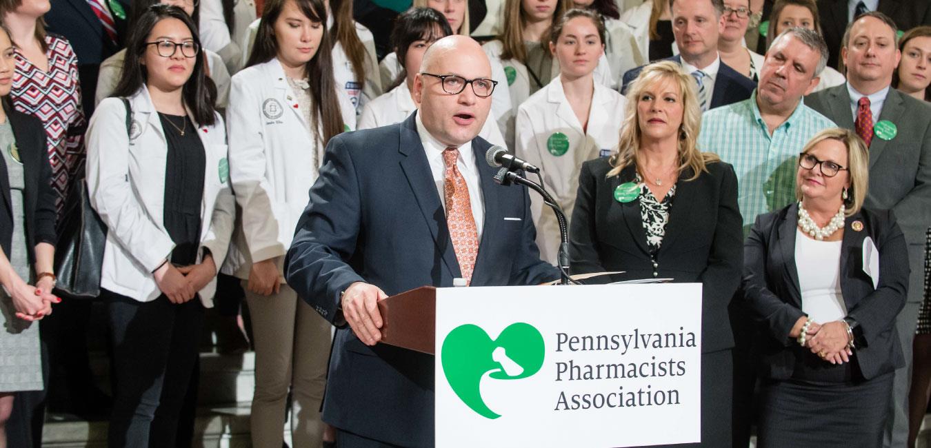 Representative Matzie speaking at podium and standing in front of Pennsylvania Pharmacists Association members on Capitol rotunda steps